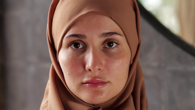 Portrait of young confident woman wearing hijab, she looks serenely and confidently straight into the camera. Indoor colose up face shot with blurred background