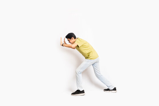 The single skinny young male tries to push something sideways. The full body of an Asian or Indonesian person. Isolated photo studio with white background.