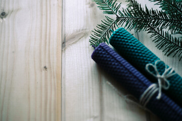 Two candles of blue and green color, tied with a tourniquet, fir branches on a light wooden background. Top view