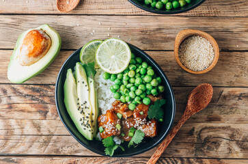 Buddha bowl with crispy sesame chicken asian style. Sweet and sour fried chicken with steamed rice, peas and acocado