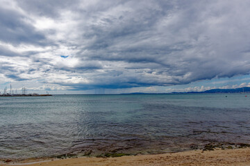 Tourists relaxing at beach S’Arenal of Mallorca Island and swimming in the ocean with mountain panorama in the background on a blue cloudy autumn day. Photo taken October 12th, 2022, Mallorca, Spain.
