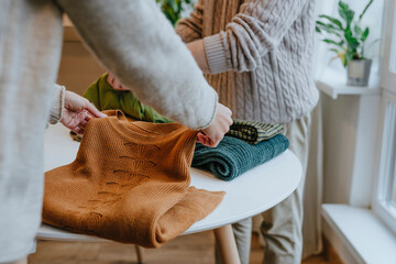 Young fashion designer with colleague folding clothes on table