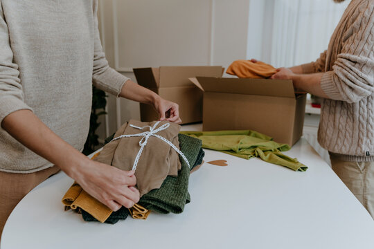 Fashion designer with colleague tying ribbon on folded clothes in workshop
