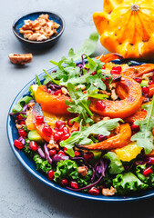 Healthy salad with baked pumpkin slices, red cabbage, avocado, lettuce, arugula, pomegranate and nuts. Vegan vegetarian eating, comfort food. Gray table background. Top view