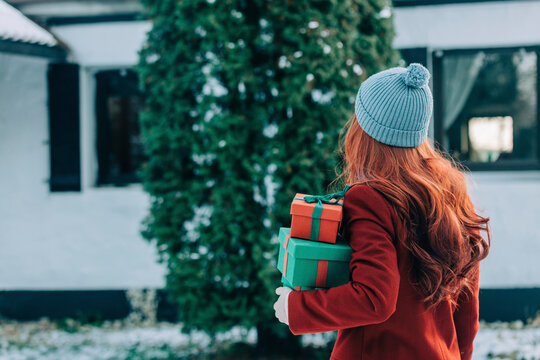 Redhead woman holding Christmas gifts standing in front of tree