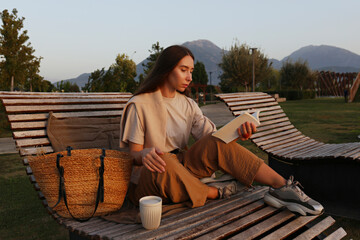 Young woman with coffee cup reading book on deck chair