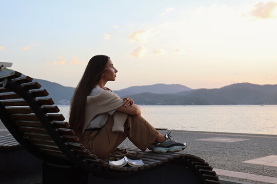 Thoughtful Woman Sitting On Deck Chair At Sunset