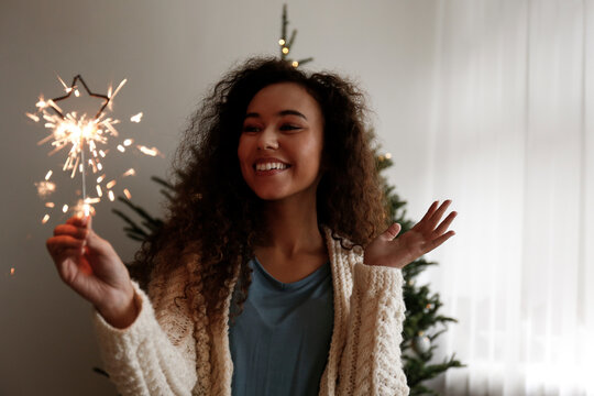 Happy woman holding sparkler standing in front of Christmas tree