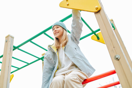 Happy teenage girl sitting on monkey bars at playground