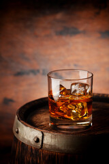 Glass of whiskey with ice cubes on the old barrel
