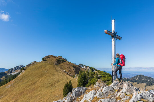 Germany, Bavaria, Female hiker touching summit cross on Kaserwand mountain