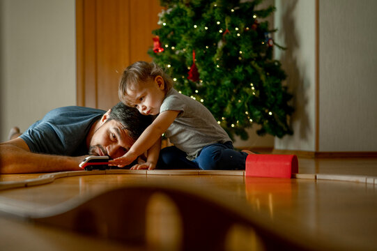 Son and father playing with toy train in front of Christmas tree