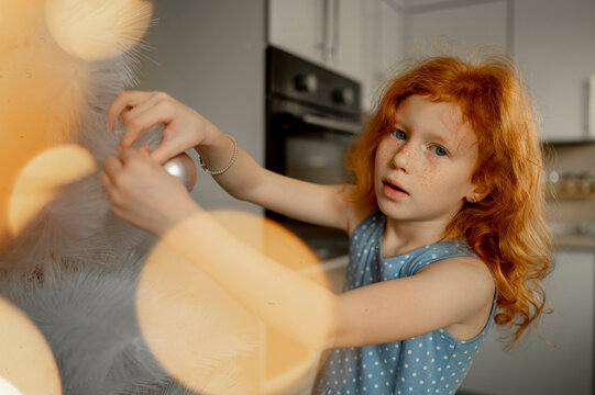 Redhead girl decorating Christmas tree with ornament at home