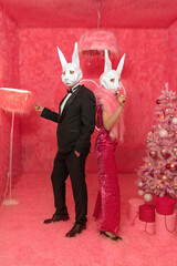 The couple in poligonal rabbit masks closeup on the pink background are celebrating New 2023 year. Celebration party