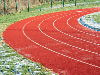 Running track partially covered with ice and snow. Dangerous surface conditions in winter cold season. Nobody. Sport training area.