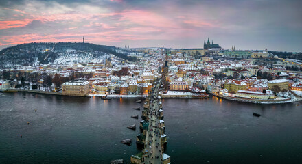 Panoramic aerial view of the snow covered cityscape of Prague, Czech Republic, with Charles Bridge and the old town during winter sunset time
