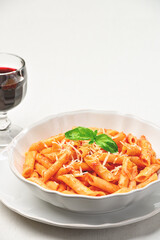 Close-up of a plate of Arrabbiata penne pasta on a linen tablecloth and a glass of red wine. Copy space. Vertical frame. Studio shot. High angle view.