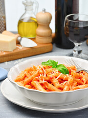 A plate of All'Arrabbiata penne pasta with basil and some cooking ingredients on the kitchen table. High angle view. Vertical frame.