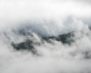 A window opens amongst the dense fog revealing forested slopes