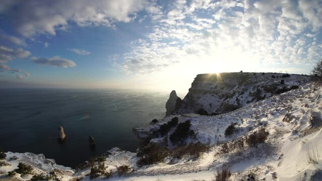 Snow covered rocky cliffs over sea. Winter landscape over the sea bay. Juniper tree under snow. Concept of winter holidays, travel and recreation. Cape Fiolent in Balaklava, Sevastopol, Crimea