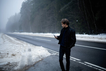 man on the road in the forest uses a smartphone.