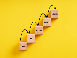 Business career path for growth and success concept. Wooden block ladder with the message take it to the next level with stepping up arrows. - obrazy, fototapety, plakaty