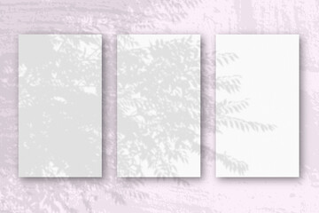 3 vertical sheets of textured white paper on soft pink table background. Mockup overlay with the plant shadows. Natural light casts shadows from an exotic plant. Horizontal orientation