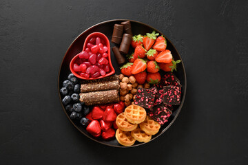 Charcuterie Valentines Day charcuterie board with chocolate, different sweets,strawberries, blueberries and candies on black background. View from above.