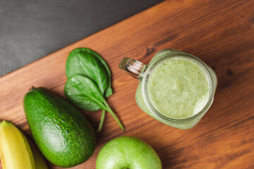 Green smoothie drink blended in a glass jar, avocado, spinach leaves, banana and apples at wooden...