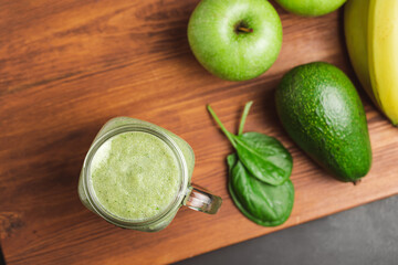 Green smoothie drink blended in a glass jar, avocado, spinach leaves, banana and apples at wooden board, top view
