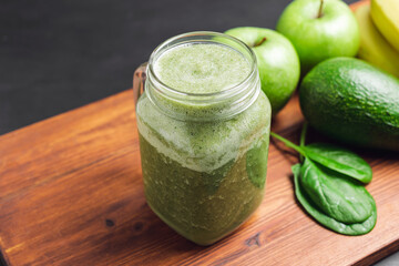 Green smoothie drink blended in a glass jar, avocado, spinach leaves, banana and apples at wooden...