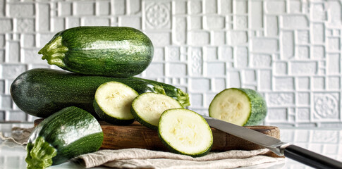 Young zucchini on a wooden board with a knife. Fresh, green vegetables on a light background, selective focus.