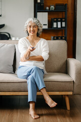 Asian old woman is watching tv and sitting on the sofa in living room at home