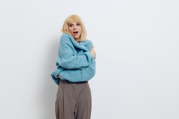 horizontal photo of a nice, sweet woman in a soft, blue sweater standing on a white background and wrapping herself in clothes with a pleasant smile on her face