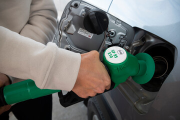 Woman hand catching green fuel nozzle into one hand while filling SP95 E10 petrol of her car in...