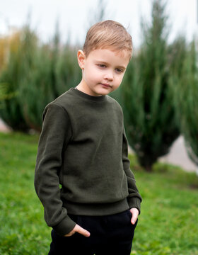 A handsome smiling boy dressed in a green sweater stands on a background of green trees. The photo is blurred