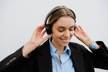 Young woman in headphones smiling while standing over white wall