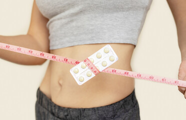 slim fit girl holding centimeter measure tape with plastic blister pack of pills tablets in...