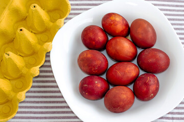 red painted eggs in cardboard holder box isolated on kitchen towel in stripes.natural dye from onion and beet bark.many eggs on white plate easter wallpaper spring is coming celebrate diy do it yourse