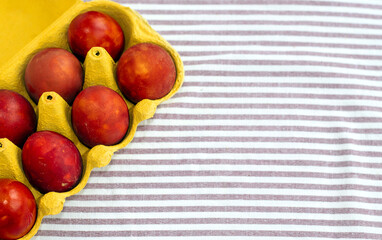 red painted eggs in cardboard holder box isolated on kitchen towel in stripes.natural dye from onion and beet bark.many eggs on white plate easter wallpaper spring is coming celebrate diy do it yourse