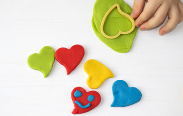 kid playing with plasticine clay making colorful hearts or holding one red heart at mouth.happy or...
