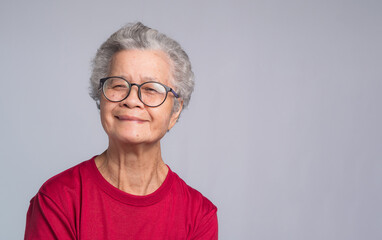 Elderly Asian woman looking at the camera with a smile while standing on a gray background