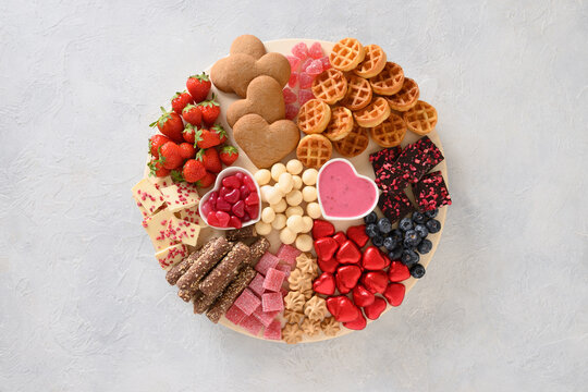 Charcuterie Valentines Day board with chocolate, red hearts, different sweets, strawberries, blueberries and candies on light gray background. View from above.