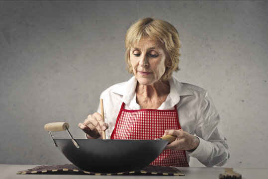 Elderly Lady Cooks With A Saucepan On A Table