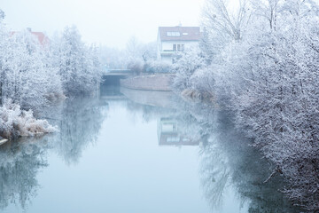 snow-covered trees along the river, reflected in the water on a fairy-tale winter day. Austria,...