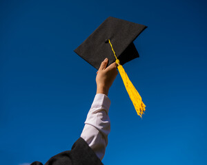 Close-up of a woman's hand with a graduation cap against the blue sky. 