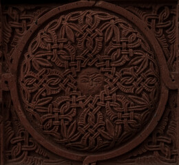 Carved round ornament with intertwining strips forming a pattern placed in a round frame on a red volcanic stone. Traditional tufa stone carving ornament on a wall of Armenian Orthodox Church.