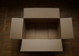 Top overhead above view photo of unpacked empty carton box on wooden floor background with blank copy space. open empty rectangular brown cardboard box for transportation and packaging of goods.