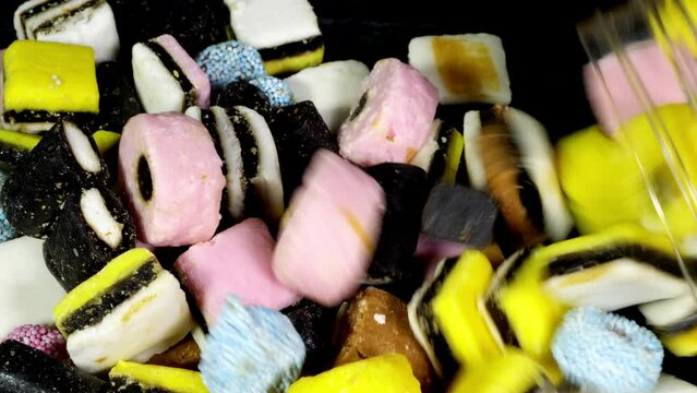 Closeup of licorice / liquorice sweet candy assortment being poured from a storage jar into a pile, ready to eat.