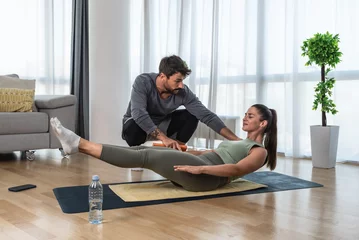 Foto op Canvas Young business woman hiring private personal fitness trainer or coach to train her in her apartment. Woman with health issue after car crash accident exercising at her home with friend helping her. © Srdjan